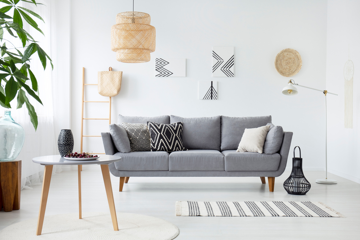 Real photo of a simple living room interior with cushions on gray sofa, paintings on white wall and cherries on a coffee table